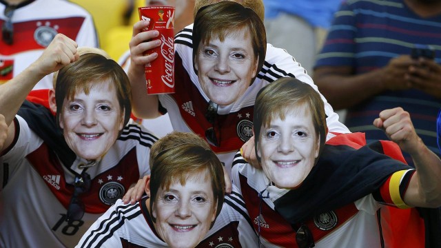 Torcedores com as máscaras da primeira ministra alemã