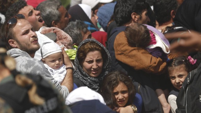 Imigrantes carregam seus filhos ao tentar embarcar em trem na fronteira da Grécia com Macedônia