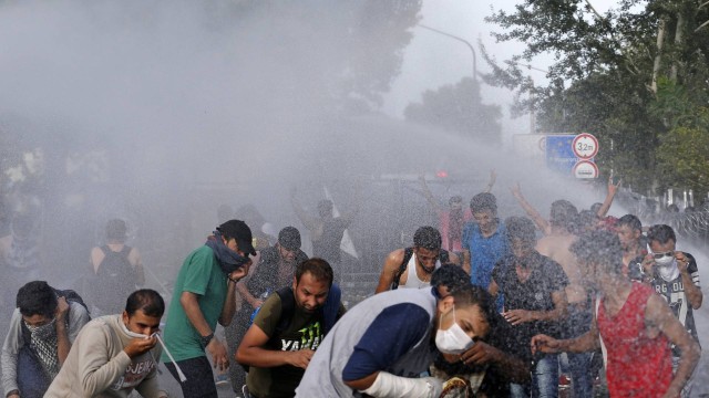 Imigrantes se protegem após a polícia húngara lançar canhões de água e gás lacrimogêneo