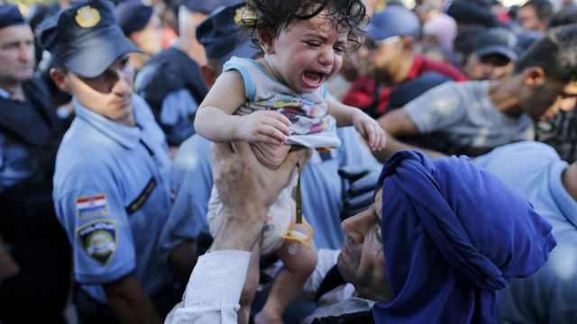 Imigrante levanta criança chorando enquanto espera por ônibus na cidade croata de Tovarnik