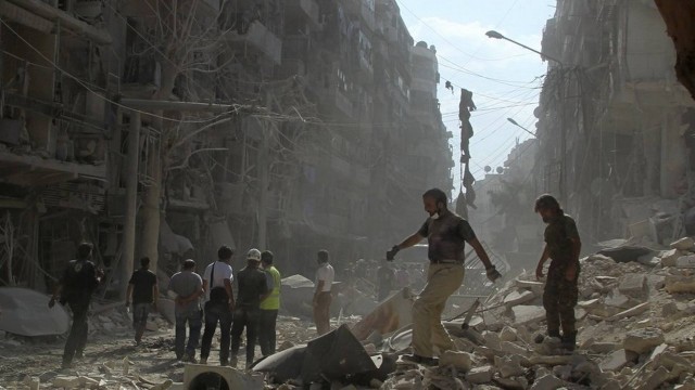 Vida sobre ruínas. Moradores e membros da defesa civil caminham pelo bairro Al-Shaar, em Aleppo: destruição total
