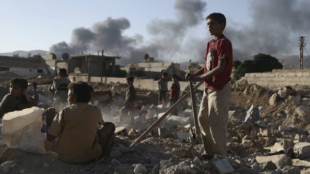 Crianças caminham sobre escombros após confrontos entre forças leais ao governo e a milícia islamista Exército do Islã, próximo à cidade de Douma, Leste da Síria