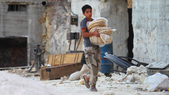 Um menino sírio carrega sacos de pães em meio a escombros após ataque aéreo russo atingir a cidade de Latamneh, no norte de Hama