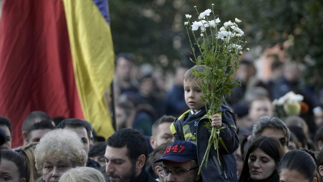 Uma criança carrega flores enquanto milhares de pessoas marcham em homenagem às vítimas do acidente em uma boate de Bucareste