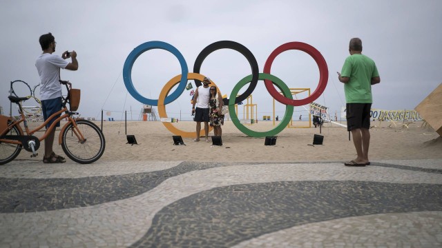 Turistas tiram fotos dos anéis olímpicos que decoram a praia de Copabana, no Rio de Janeiro