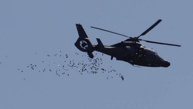 Helicóptero militar joga panfletos para os moradores da Rocinha com telefone para denúncias contra o tráfico