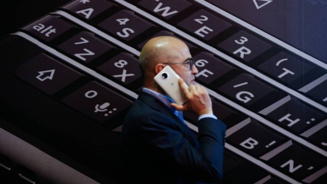 Uma pessoa usa seu dispositivo móvel enquanto passa por um pôster do smartphone Blackberry Keyone, fabricado pela Blakberry, no segundo dia do Mobile World Congress (MWC) em Barcelona, em 2017