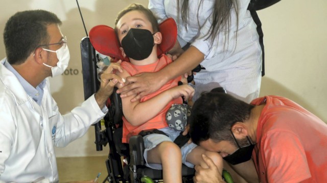 O menino Davi é vacinado ao lado do pai, Paulo Silva, que se emociona e chora