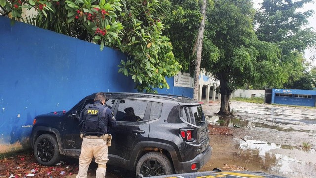 Policial rodoviário federal observa um dos veículos encontrados no pátio do Ciep na Maré