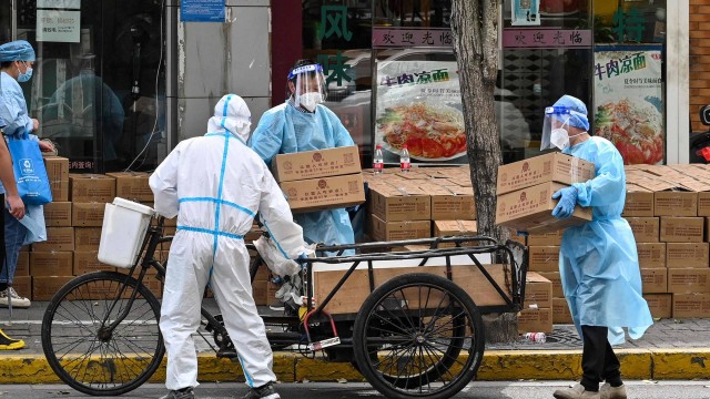 Trabalhadores usando equipamentos de proteção empilham caixas sobre um carrinho de entrega durante uma quarentena de Covid-19 em Xangai, na China