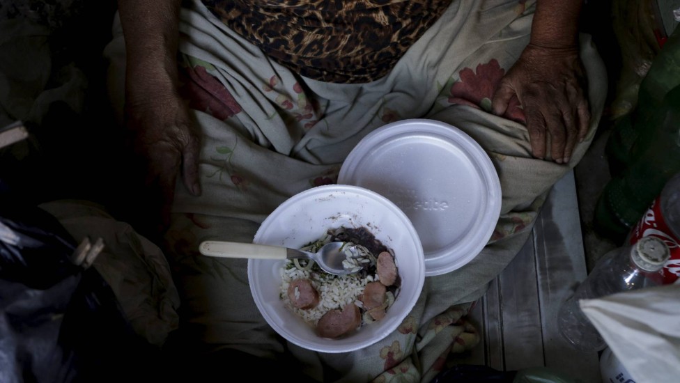 Dona Juraci da Silva, 73 anos, come uma quentinha doada pela igreja. A idosa mora em um barraco às margens da linha verde, em Acari.