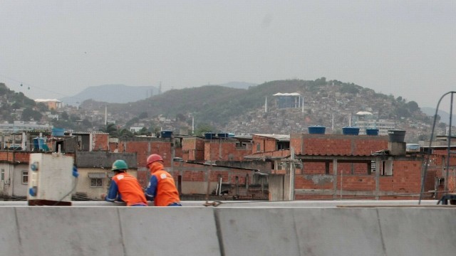 Funcionários da obra da ponte observam o Complexo da Maré, com o teleférico do Complexo do Alemão ao fundo